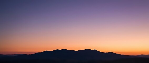 Fototapeta premium Dramatic sunset sky with vibrant purple and orange gradient colors over dark mountain silhouettes creating peaceful twilight landscape scenery.