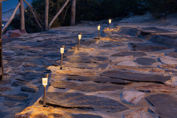 A rustic stone pathway is illuminated at dusk by a series of small solar-powered garden lights...