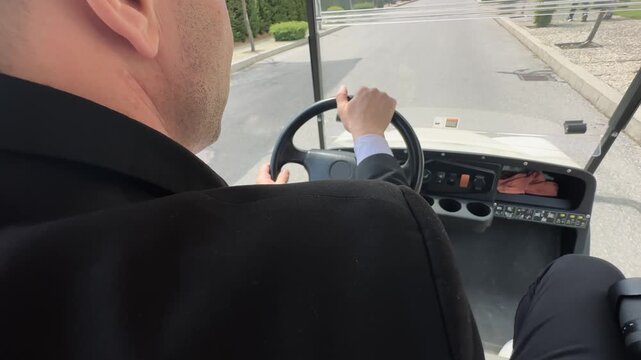 Unrecognizable service man driving golf cart around the park in sunny summer day