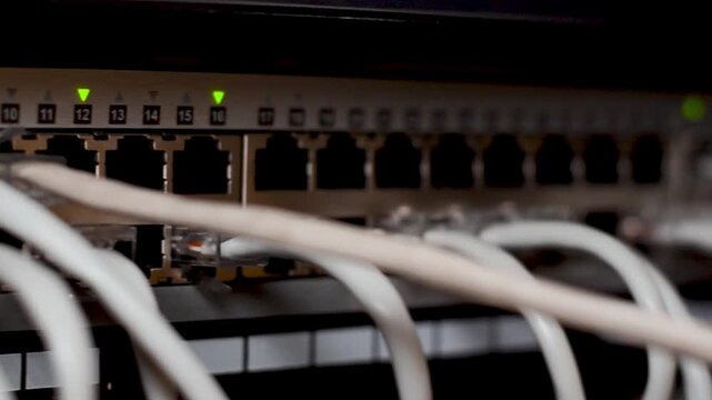 Server room rack with network cables. Network cables connect to server rack ports with blurry bokeh lights in the background. A close-up of a network rack with multiple Ethernet cables connected to it