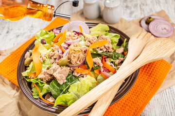 Bowl of colorful tuna salad with various vegetables and wooden serving utensils.