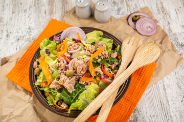 A plate of colorful salad with tuna, which includes lettuce, grated carrot, red onion, olives and tomatoes.