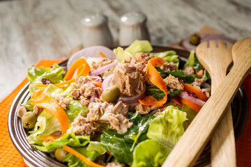 Bowl of colorful tuna salad with various vegetables and wooden serving utensils.