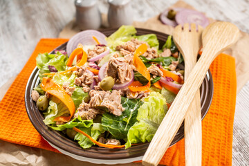 Bowl of colorful tuna salad with various vegetables and wooden serving utensils.
