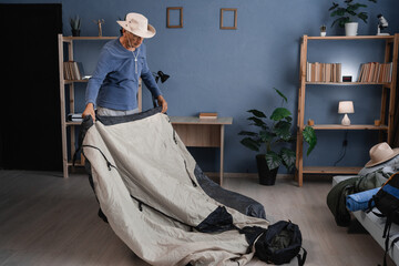 Active senior traveler preparing trekking equipment and tent for journey