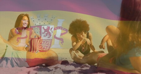 Laughing friends wearing swimsuits and sunglasses reclining on sandy beach, Spain flag overlay
