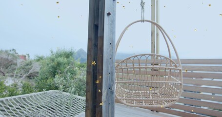 Swaying woven rattan egg chair hanging from overhead beam on beachfront deck, with net hammock