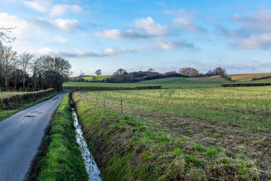 A country road running alongside farmland in Sussex, with a ditch full of water after rainfall