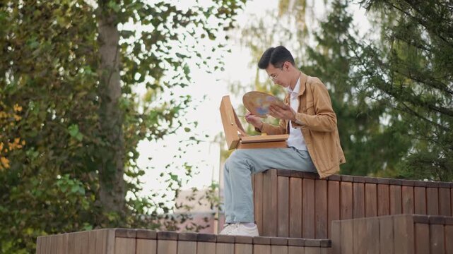 Young white man planning journey outdoors, travel blogger and aspiring cartographer studying vintage globe on wooden steps, sketching routes and itineraries, sunlight filtering through trees, casual