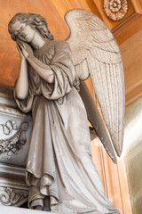 Antique statue in old European cemetery. Angel praying and covered by dust.