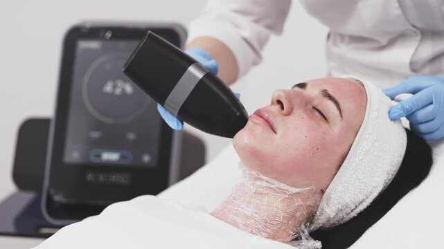 Female patient receiving advanced microneedle RF facial treatment at aesthetic clinic. Skin firming, collagen renewal and professional dermatology procedure.