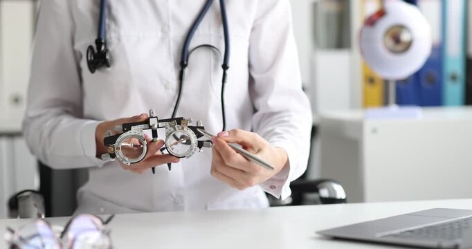 Ophthalmologist holds trial frame adjusting lenses for vision test. Woman explains glasses importance showing trial frame elements at appointment