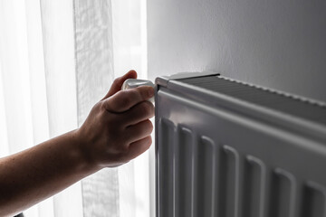 Hand adjusting radiator. Regulation control of the heating temperature on the battery in the room, female hand. Adjusting turn on heating up, thermostatic radiator valve on radiator.