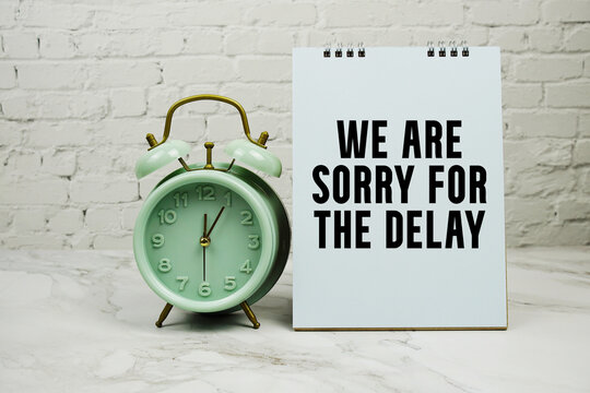 We Are Sorry For The Delay with green vintage alarm clock against a white brick wall background.
