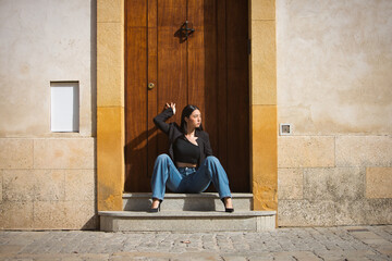 Young woman, attractive, brunette, blue eyes, Hispanic, wearing a black jacket and top, jeans, posing while sitting on the sill of a beautiful doorway. Concept: model, beauty, fashion, trendy.
