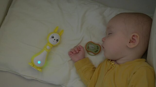 caucasian baby sleeping beside glowing toy and pacifier, dreaming sleeper in yellow onesie on soft pillow with gentle nightlight glow, serene nap routine, tranquil nursery ambiance