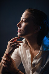 Thoughtful in harsh studio light: portrait of a woman with an expressive gaze in a shirt against a blue background