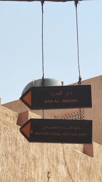 Direction signs in Arabic and English hang against a traditional wall, directing visitors to the Architectural Heritage Department and Dar al-Nadwa in Al Seef, Dubai, vertical video
