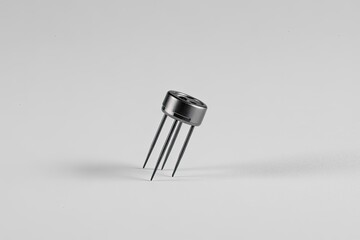 Small metallic electronic component with three pins, round shape, silver and black, isolated on white