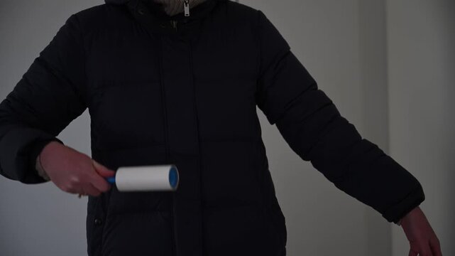 Woman removing pet hair from winter jacket using lint roller at home, fabric care concept