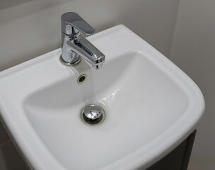 Fototapeta premium A clean, white ceramic bathroom sink with a polished chrome faucet and drain fitting is shown from above.