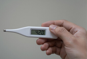 An adult hand holds a digital thermometer displaying a critically high temperature reading of 42.0.