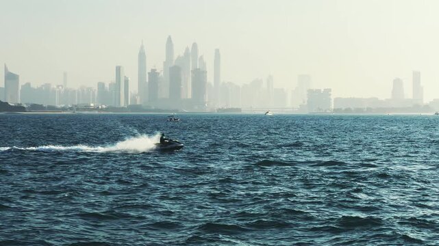 Man ride motor jet skiing on vibrant waters near modern skyline of Dubai Marina during sunset, no logos