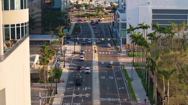 Aerial view of Sarasota city center intersection with multiple lanes, vehicles stopping, and groups of pedestrians moving across crosswalk during rush hour.