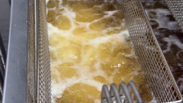 Cooking oil bubbles in deep fryer with metal basket, showcasing the frying process in a commercial kitchen setting