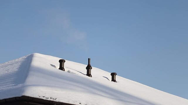 Steam slowly rises from a snow-covered roof vent on a cold, sunny winter day against a clear blue sky