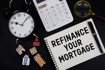 Notepad with the phrase "Refinance Your Mortgage" surrounded by a pen, calculator, magnifying glass, clock, and house model