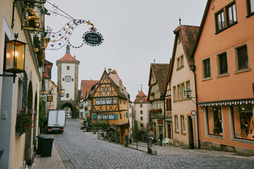 Obraz premium Cobblestone street in Rothenburg ob der Tauber lined with half-timbered houses, a clock tower, and ornate wrought-iron sign for Goldener Hirsch