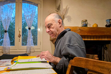 An elderly man sorts through papers at a table at home setting