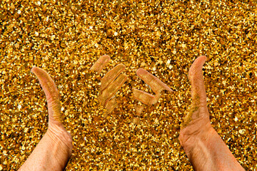 hands immersed in golden sand show gold particles