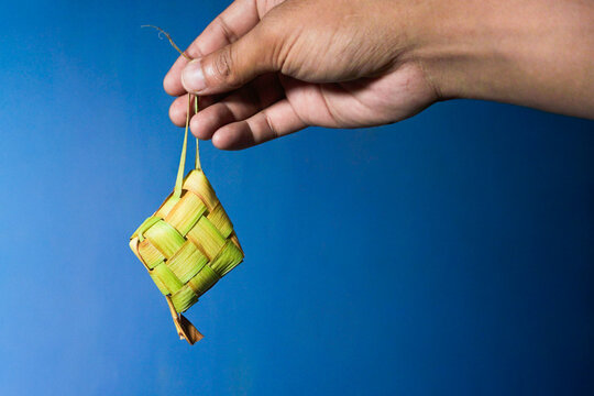 Hand hold Ketupat or rice cake is served on a white plate on white. Traditional Indonesian food at Eid al-Fitr