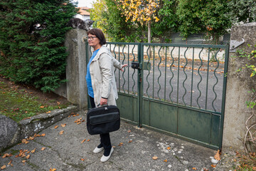 A woman holds a bag while standing by a green gate in autumn