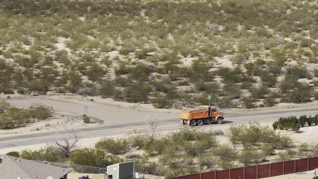Aerial following orange trash dump truck in Arizona desert on paved road
