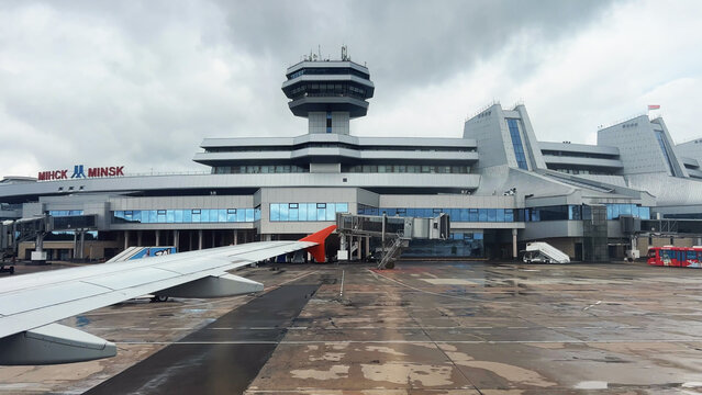 Minsk, Belarus - August 21, 2024: Airplane wing near passenger boarding bridge at minsk national airport terminal on a cloudy day