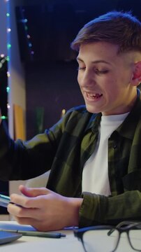 Smiling funny boy playing online game with smartphone by sudden victory, celebrate while sitting on dask at home. New generation new generation games. Slow motion.