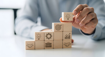 Hand arranging wooden blocks like steps, business icons visible, clean focus, soft blur background, strategic planning concept