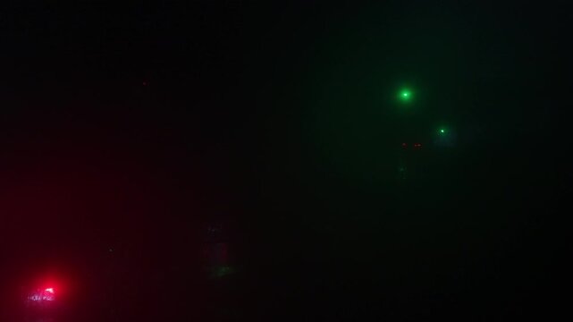 Elevated view of foggy night traffic as cars move and stop at a signalized intersection. Atmospheric urban transport scene showing motion, control, and city life after dark.