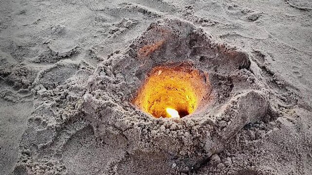 A high angle close up shot video of a hole dug in the beach sand filled with burning candles during the iemanja celebration