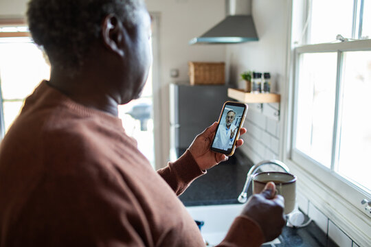 Senior man having telehealth video call at home kitchen