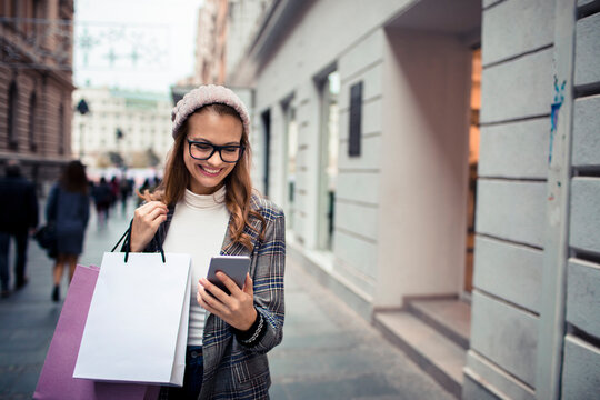 Smiling woman with shopping bags using smartphone on city street