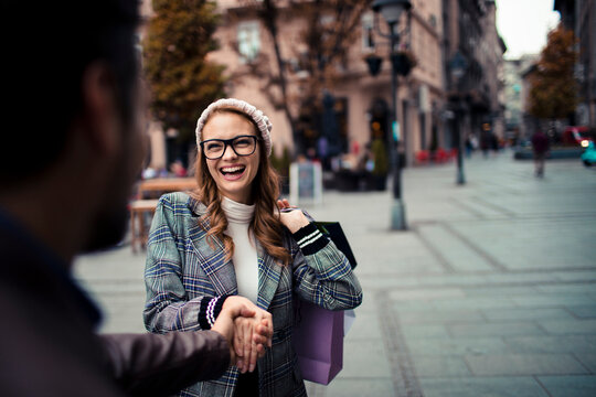 Smiling woman greeting friend on city street with shopping bags