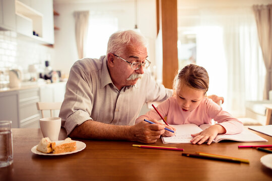 Grandfather helping granddaughter with homework at kitchen table