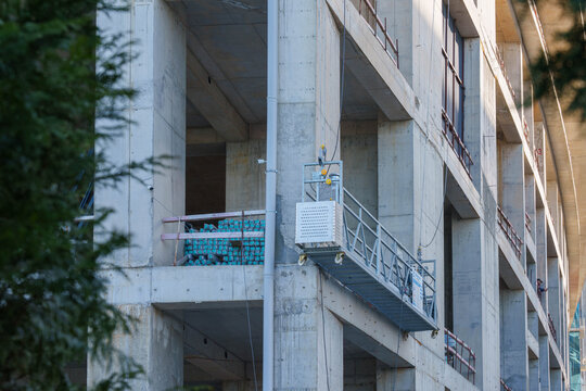 Concrete building under construction with suspended scaffolding platform and safety railings on upper floors
