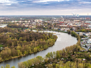 Panoramiczne ujęcie z lotu ptaka na zakole rzeki Odry w Opolu, sąsiadujące z gęsto zalesioną Wyspą Bolko, z widoczną w oddali zabudową miejską i infrastrukturą przemysłową. © Henryk Niestrój