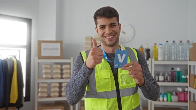 Man holds badge and gives thumbsup inside charity hall alongside hispanic young volunteer at donation center smiling.
