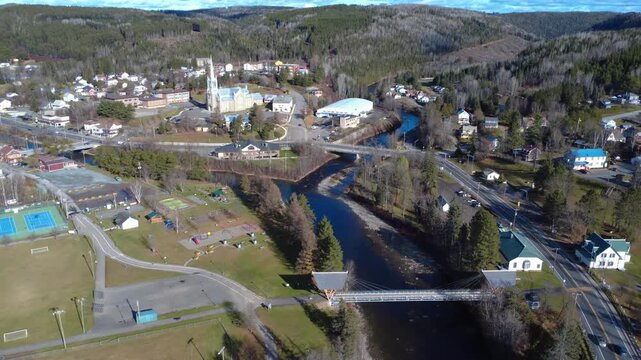 Aerial view of the sunny rural town of Causapscal bordering the Matapedia salmon river, with its church, public buildings, bridges and houses. Quebec, Canada, 2025.